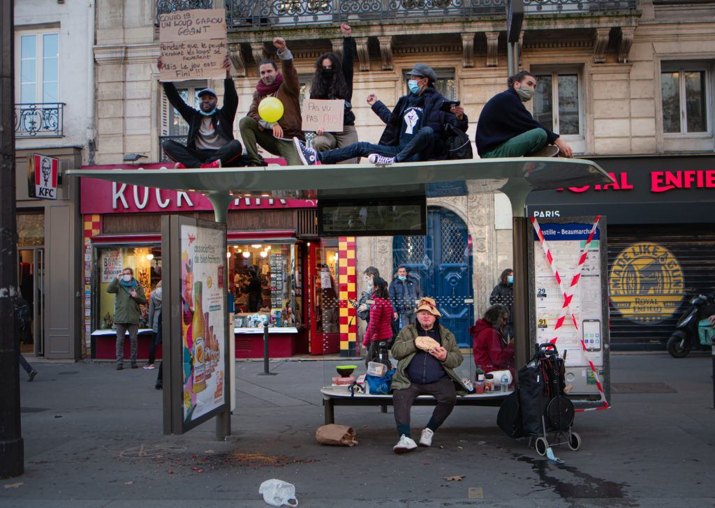 Des manifestants sur un abri-bus place de la bastille brandissant des pancartes et un homme sans abri en plein repas - 28 novembre 2020 - Manifestation contre le projet de loi Sécurité Globale