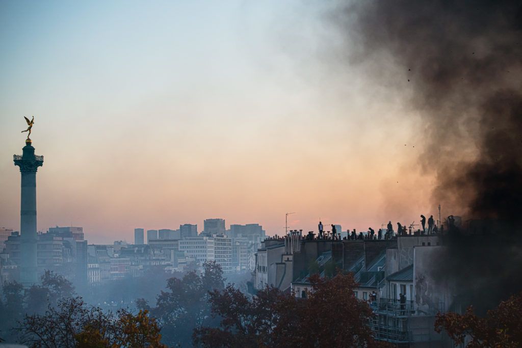 Plusieurs personnes sur un toit au dessus de la place de la bastille face au génie, dans la fumée des feus allumés durant la manifestation - 28 novembre 2020 - Manifestation contre le projet de loi Sécurité Globale - Paris
