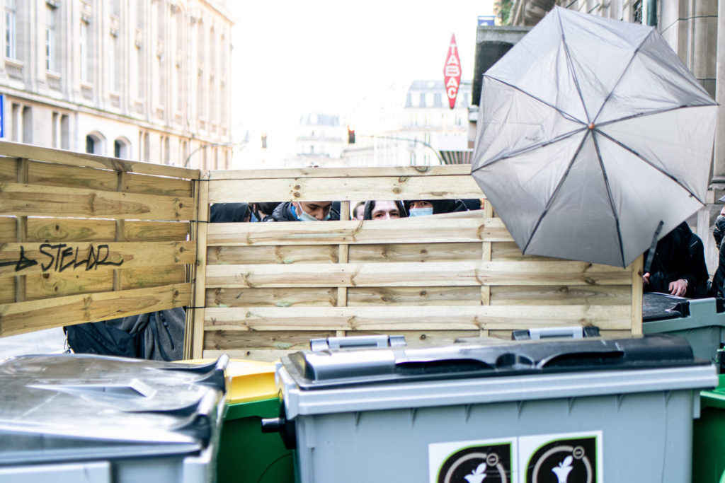 Des lycéens observent les mouvement des forces de l'ordre par les trous de leur barricade devant le lycée Racine à Paris le 26 janvier 2021