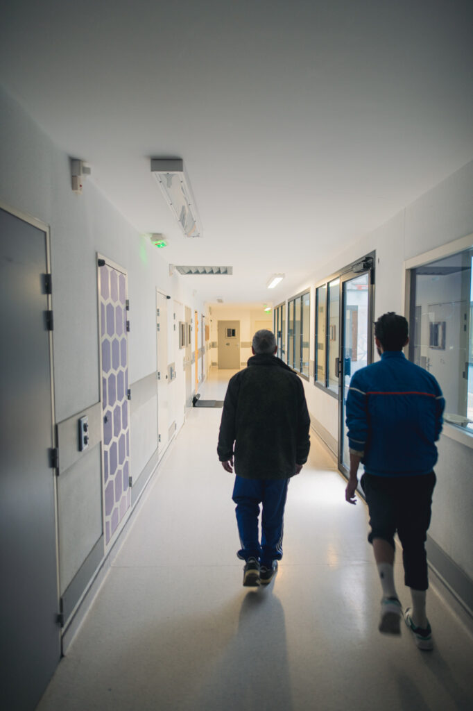 Deux patients détenus, empruntent un couloir du bâtiment Majorelle de l'UHSA de Seclin, qui accueille des personnes détenues souffrant de troubles psychiatrique et ayant fait l'objet d'une hospitalisation contrainte, pour aller fumer dans le patio.