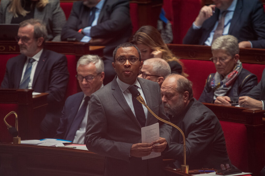 Pap Ndiaye regarde vers le haut alors que les ministres derrière lui regardent tous vers le bas, alors qu'il répond à une question le 22 novembre 2022 à l'Assemblée Nationale