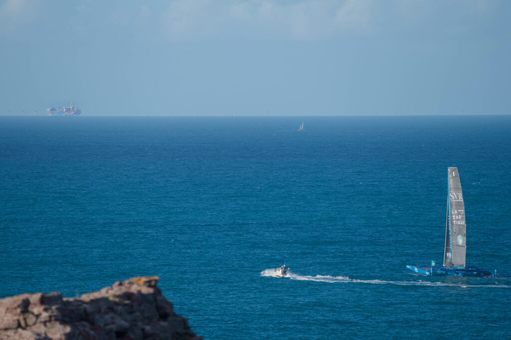 Le bateau SVR Lazartigue de François Gabard passe entre le cap Fréhel et l'usine éolienne de la baie de St-Brieuc en travaux, après le départ de la route du Rhum le 9 novembre 2022.
